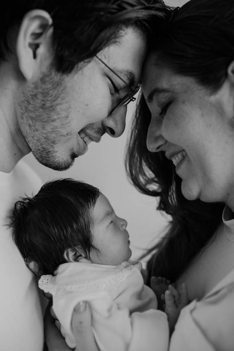 Versão em preto e branco do retrato de perfil do casal sorrindo com a bebê.'