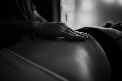 Versão em preto e branco do close focado na massagem lombar de alívio durante a contração.'