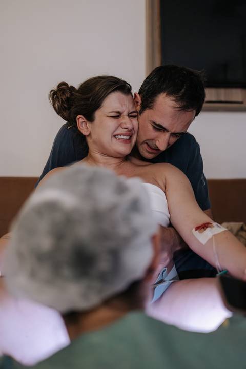 Foto do momento de força máxima da mãe, abraçada por trás pelo parceiro durante o nascimento.'