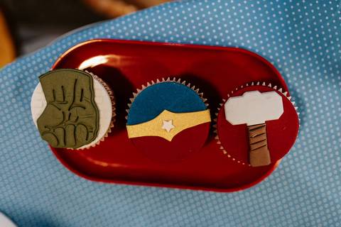 Close de doces decorados com os símbolos do Super-Homem, Mulher-Maravilha e o martelo do Thor.'