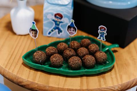 Detalhe de brigadeiros organizados em um prato verde em formato de folha, com toppers dos aniversariantes.'