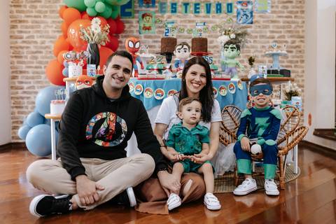 Retrato da família reunida sentada no chão em frente à mesa decorada, com o filhos fantasiados.'