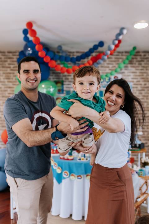Retrato do casal segurando o filho menor no colo, todos sorridentes em frente à decoração.'