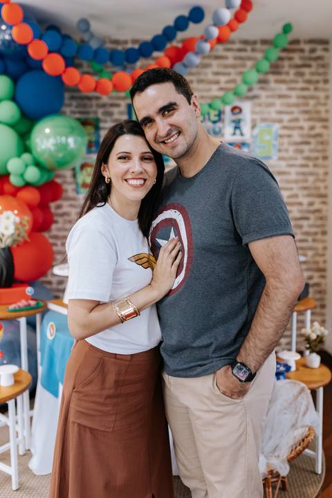 Foto aproximada do casal abraçado, destacando as camisetas com os símbolos da Mulher-Maravilha e do Capitão América.'