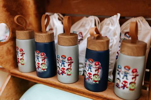 Detalhe das lembrancinhas personalizadas da festa, incluindo garrafinhas térmicas com estampas de heróis.'