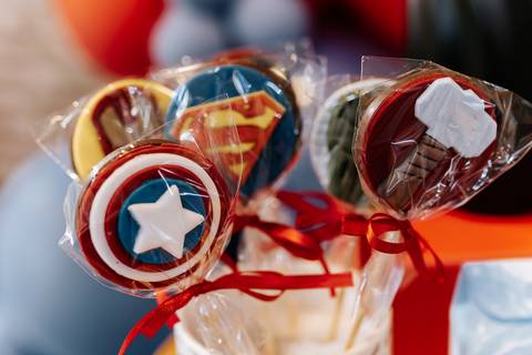 Close de pirulitos de chocolate artesanais decorados com os escudos do Capitão América e do Super-Homem.'