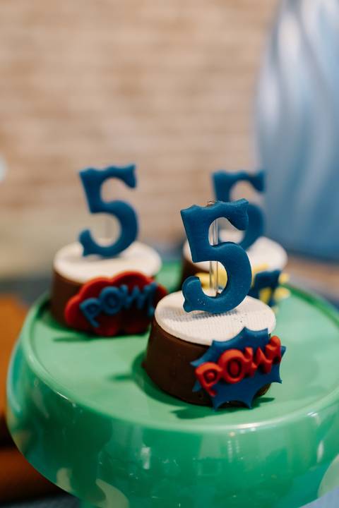 Foco aproximado nas velas azuis de número 5 no topo de cupcakes personalizados.'