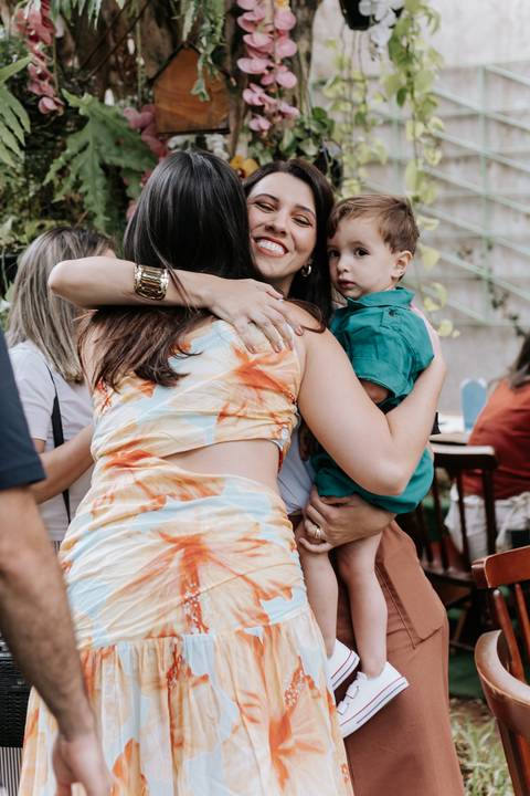Registro espontâneo de um abraço carinhoso recebido pela mãe enquanto segura o filho menor no colo.'
