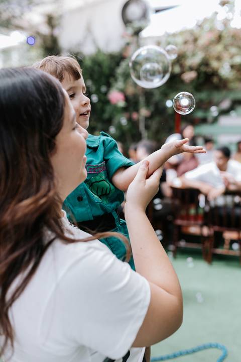 Foto da convidada brincando com o aniversariante e bolhas de sabão. '