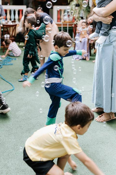 Foto em movimento do aniversariante fantasiado correndo e se divertindo em meio a bolhas de sabão.'