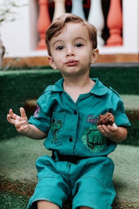 Close aproximado do aniversariante mostrando a mão suja de chocolate enquanto segura um doce.'