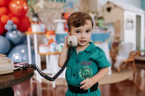 Registro divertido do caçula segurando o gancho de um telefone antigo de brinquedo perto do ouvido.'