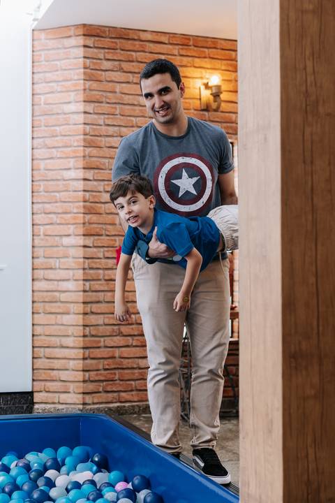 Foto do pai segurando o filho mais velho de pontacabeça nas costas, em momento de pura brincadeira.'