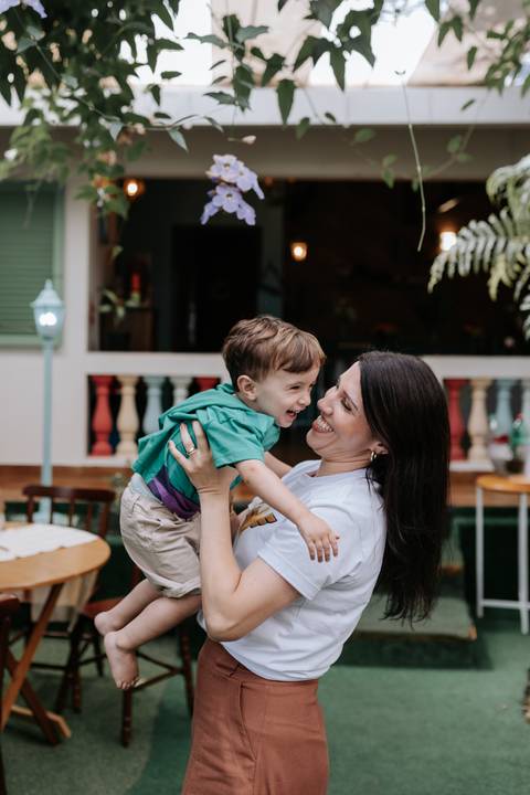 Foto da mãe com um sorriso radiante, segurando o filho caçula no colo em um momento de chamego.'