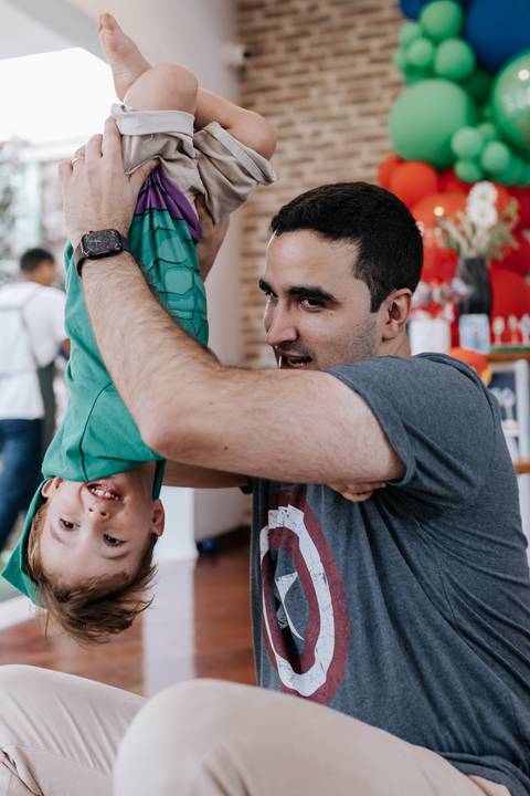 Foto divertida do pai virando o caçula de pontacabeça no ar, com os dois rindo muito.'