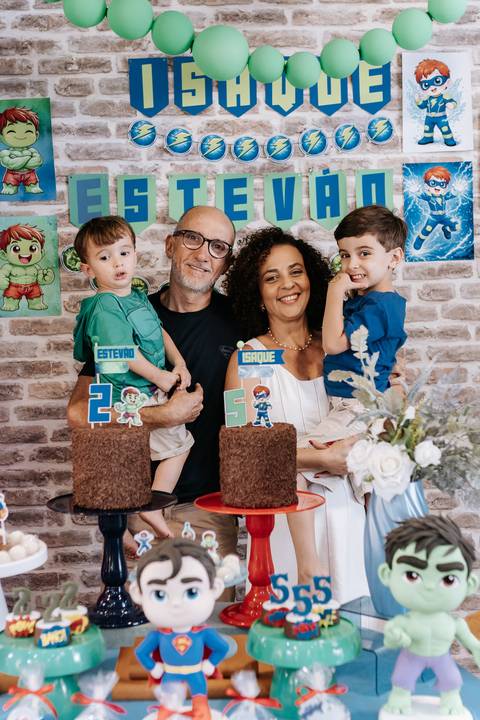 Retrato carinhoso dos aniversariantes com os avós, posando atrás dos bolos de chocolate com toppers.'