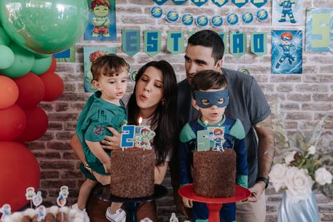 Registro da mãe ajudando os aniversariantes a soprarem as velinhas de 2 e 5 anos nos bolos de chocolate.'