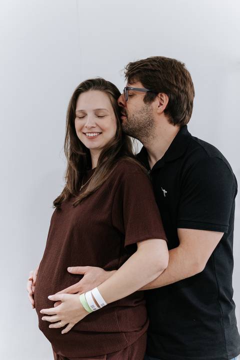 Foto aproximada da gestante recebendo um beijo carinhoso do parceiro no rosto.'