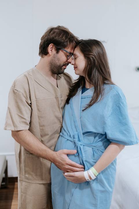 Retrato do casal já com as roupas cirúrgicas, trocando um momento de carinho antes do procedimento.'