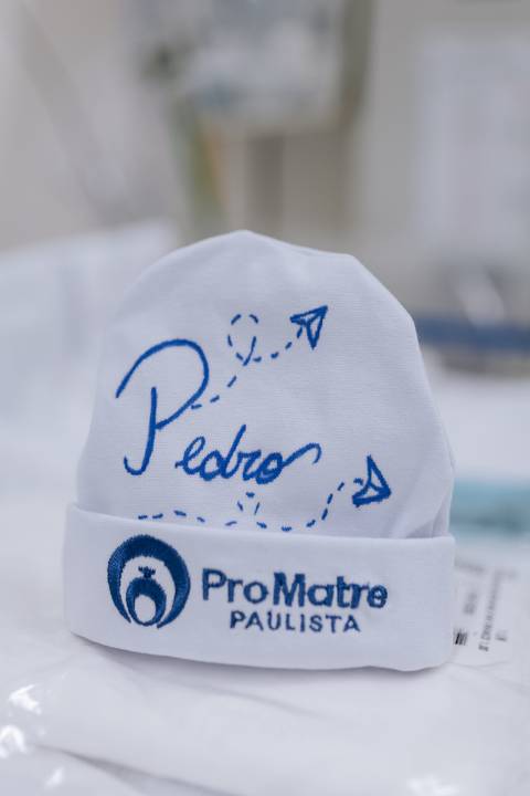 Close-up focado no detalhe da touquinha branca personalizada com o nome 