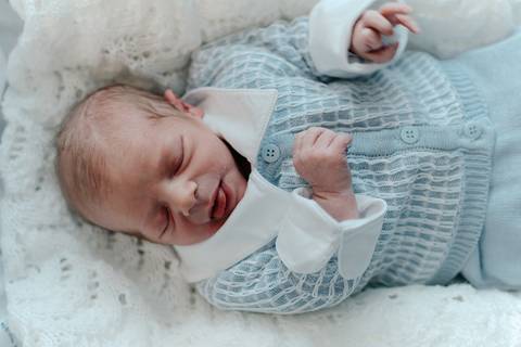 Foto aproximada do bebê Pedro dormindo com a cabeça virada de lado, vestindo a saída de maternidade.'