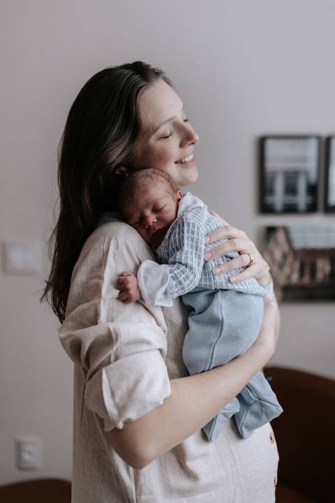 Foto de perfil da mãe em pé, abraçando e ninando o pequeno Pedro adormecido em seu ombro.'