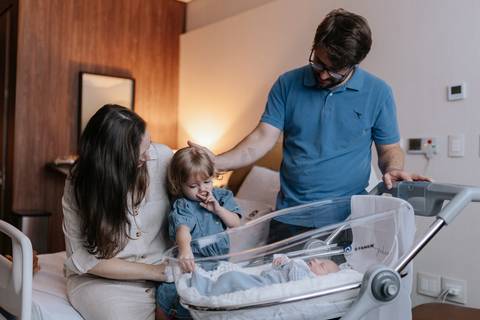 Foto do casal com a filha mais velha conhecendo o irmãozinho. '