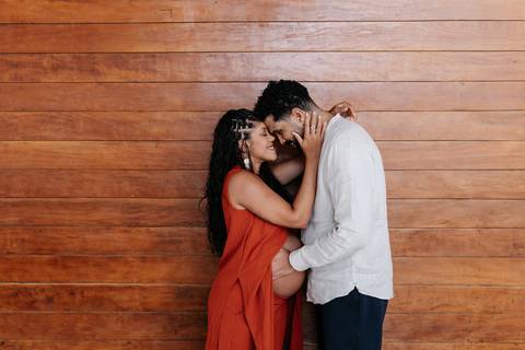Retrato íntimo do casal encostando as testas com carinho, com o painel de madeira ao fundo.'