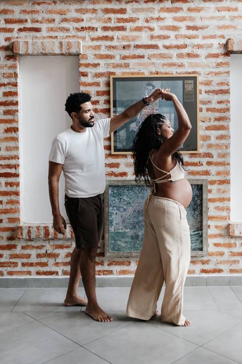 Registro divertido e dinâmico do casal dançando e sorrindo no meio da sala decorada.'