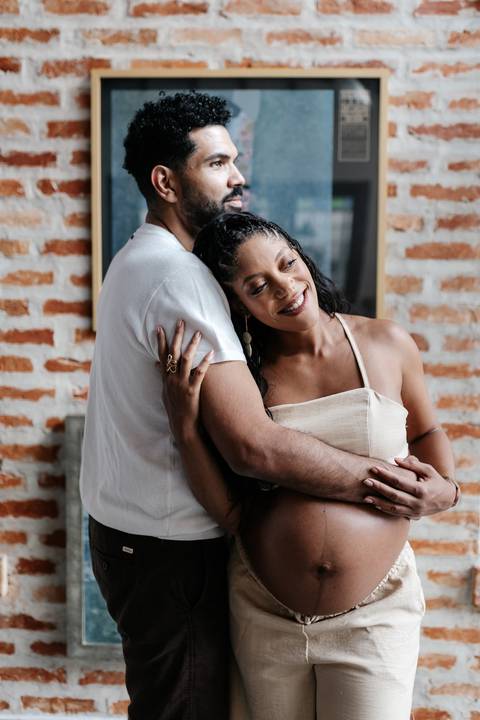 Retrato aproximado do parceiro abraçando a gestante por trás em um momento intimista e acolhedor.'