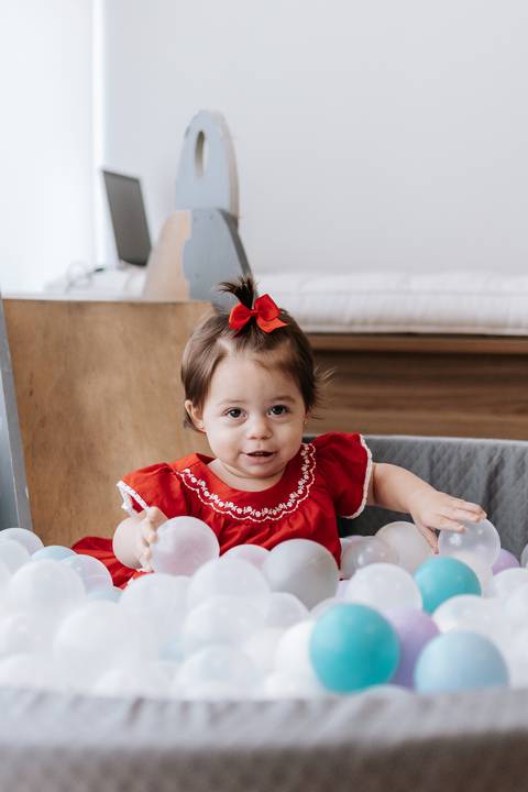 Bebê sorrindo na piscina de bolinhas da festa.'