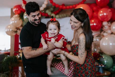 Pais fazendo cócegas e brincando com a bebê na festa.'