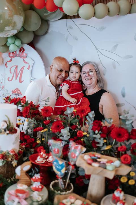 Aniversariante no colo dos avós maternos perto da decoração.'