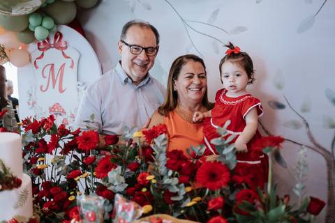 Bebê com os avós paternos sorrindo atrás da mesa principal.'