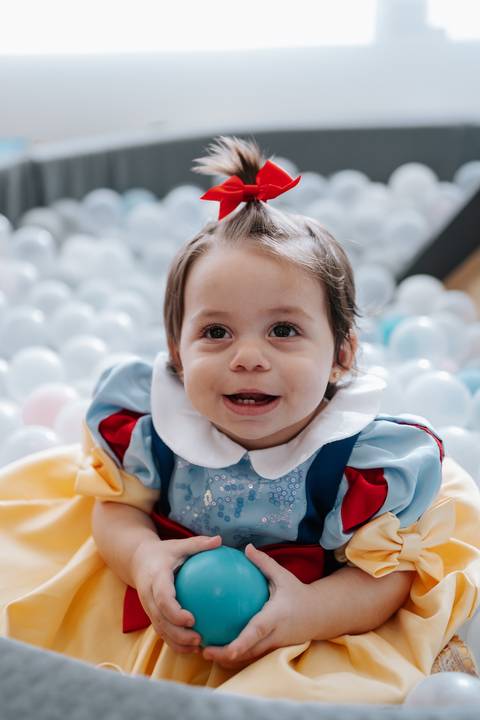 Close da bebê sorrindo com a fantasia de Branca de Neve na piscina de bolinhas.'