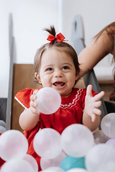 Close da bebê radiante segurando uma bolinha branca na piscina.'