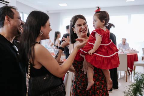 Mãe com a aniversariante no colo conversando e interagindo com os convidados.'