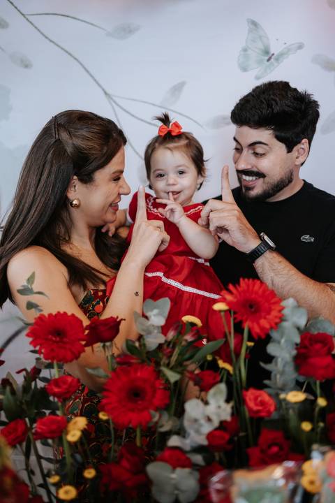 Pais sorridentes com a bebê indicando o número um com o dedinho.'