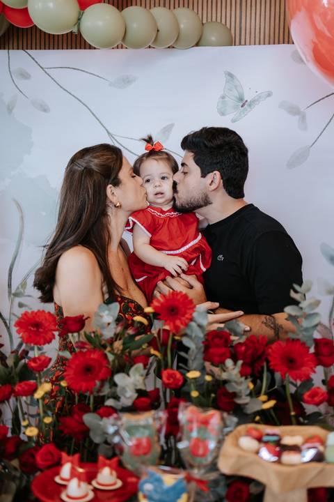 Retrato carinhoso do casal dando beijinhos nas bochechas da filha.'