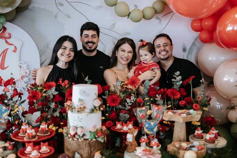 Retrato oficial com os pais e convidados reunidos atrás da mesa do bolo.'