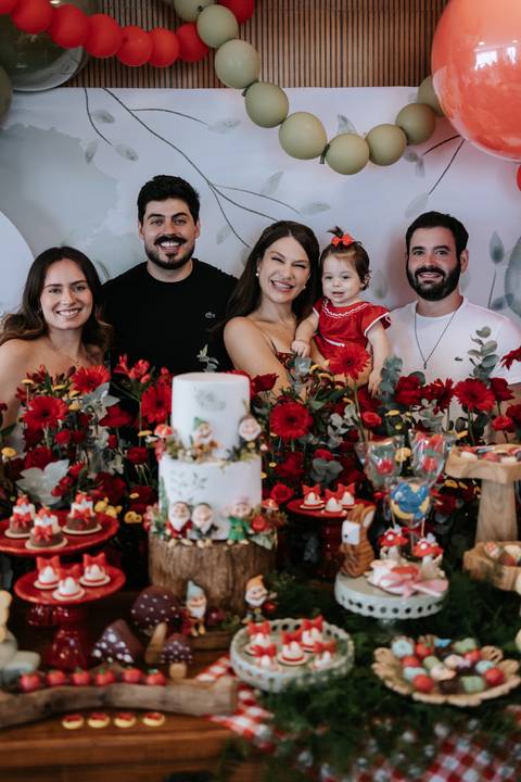 Retrato dos pais com familiares reunidos ao redor da mesa do bolo.'