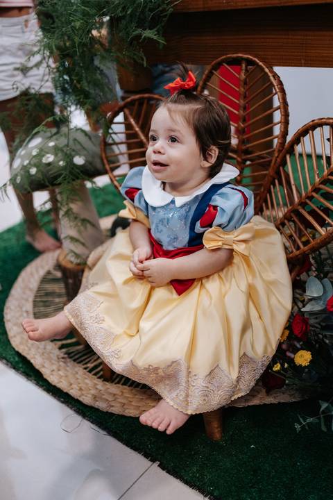 Close da aniversariante de saia amarela sentada no chão olhando para o lado.'