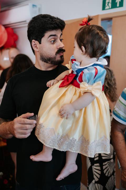 Detalhe do pai segurando a bebê no colo, destacando o laço da fantasia.'