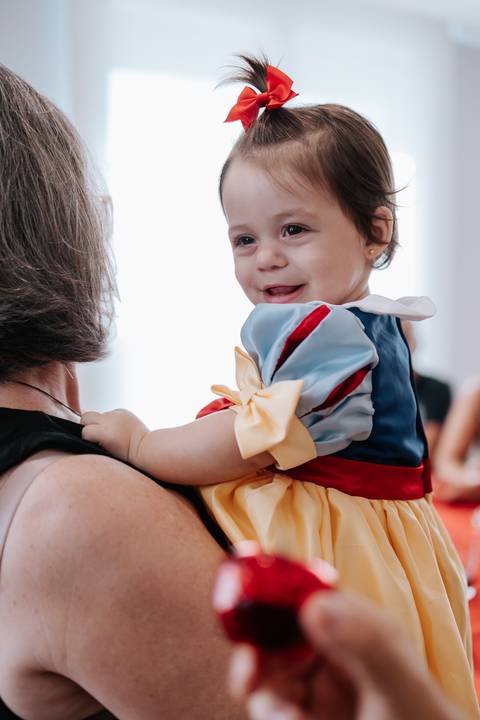 Bebê no colo de uma convidada olhando para trás com expressão curiosa.'