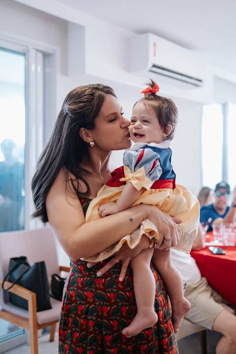 Registro carinhoso da mãe dando um beijo na bochecha da filha fantasiada.'