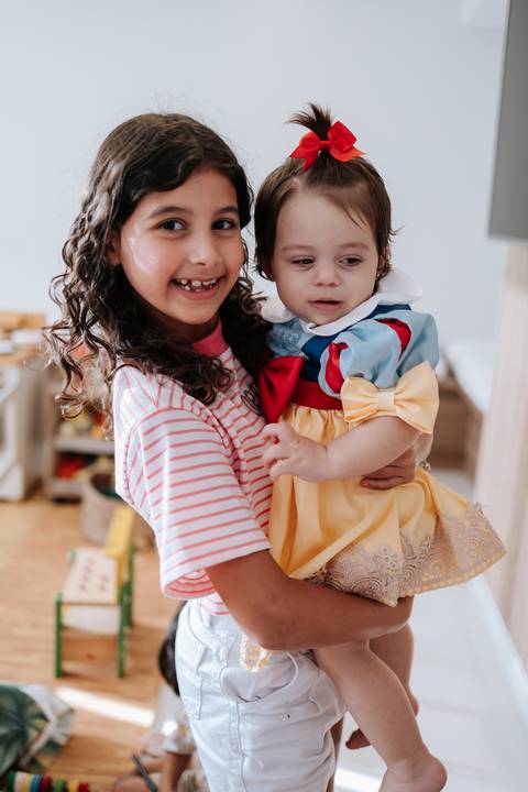 Criança maior segurando a aniversariante no colo e sorrindo para a foto.'
