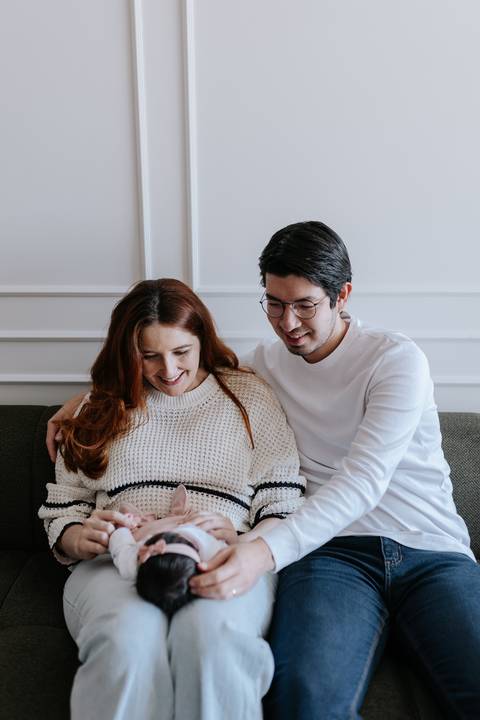 Retrato do casal sorrindo e olhando para o recém-nascido no colo da mãe.'