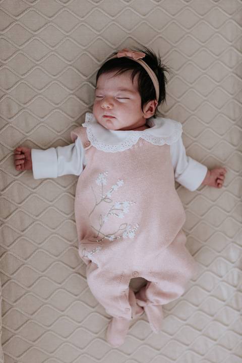 Foto da bebê Nely deitada no berço, mostrando a roupinha de tricô.'