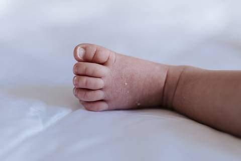 Detalhe em close focado no pezinho minúsculo da bebê sobre o lençol branco.'