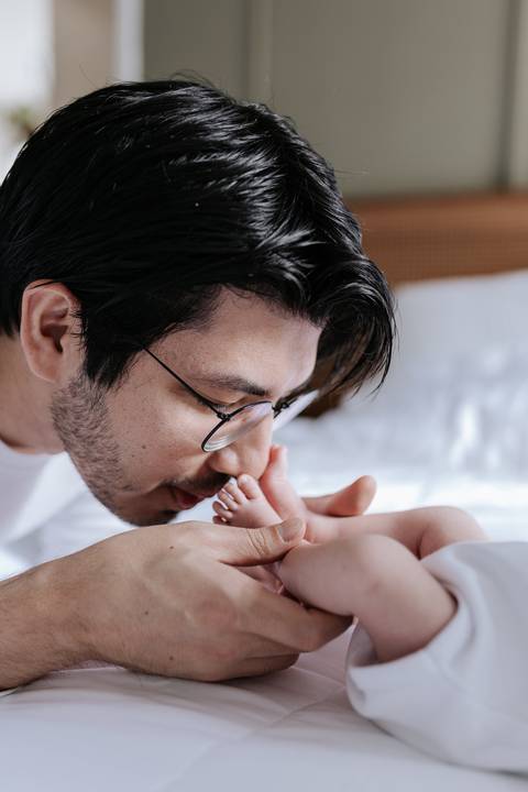 Pai beijando com carinho os pezinhos minúsculos da recém-nascida.'